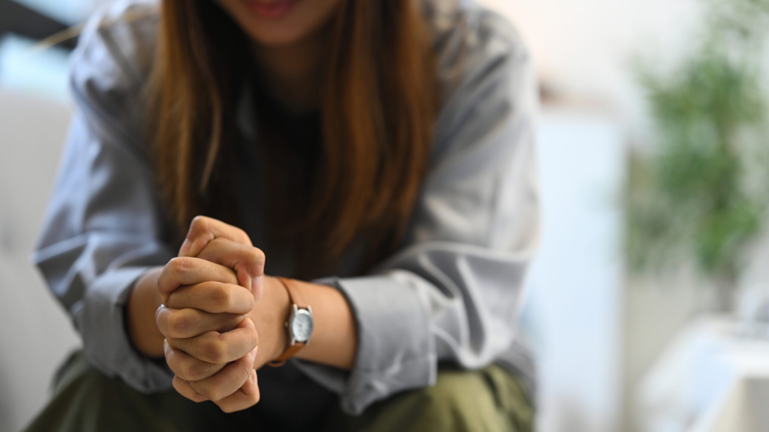 depressed,sad,woman,sitting,alone,on,sofa,with,hands,clasped.